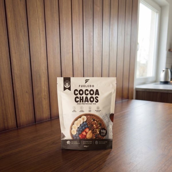 A stand-up pouch of FULLEDD Cocoa Chaos oats mix placed on a wooden table in a real indoor setting with wood-paneled walls and a window in the background.