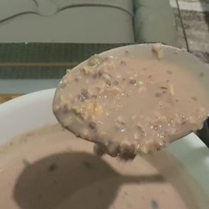 A close-up of a spoonful of Fueledo high protein oatmeal or a thick soup, held above a bowl in an indoor setting.